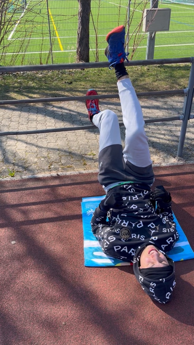 Vinicius lying on a mat on the track, raising his legs toward the railing