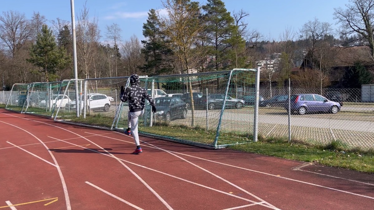 Vinicius doing leg swings on the running track next to the football goals
