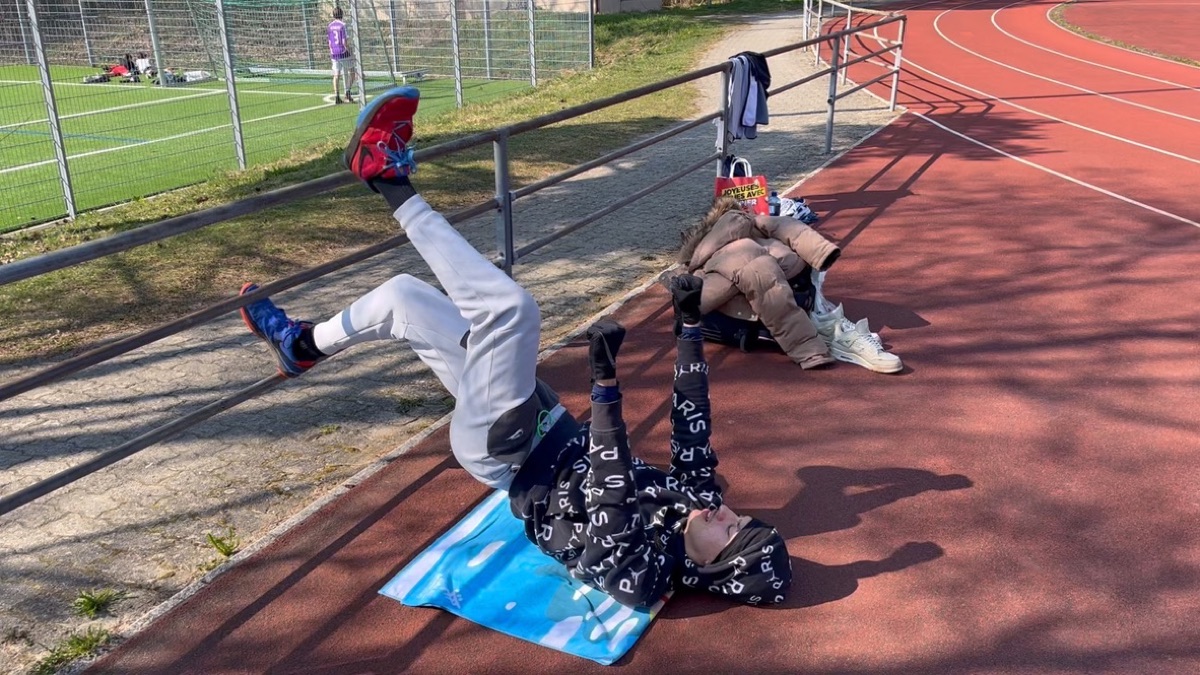Vinicius on a mat at the edge of the track, legs raised toward the railing